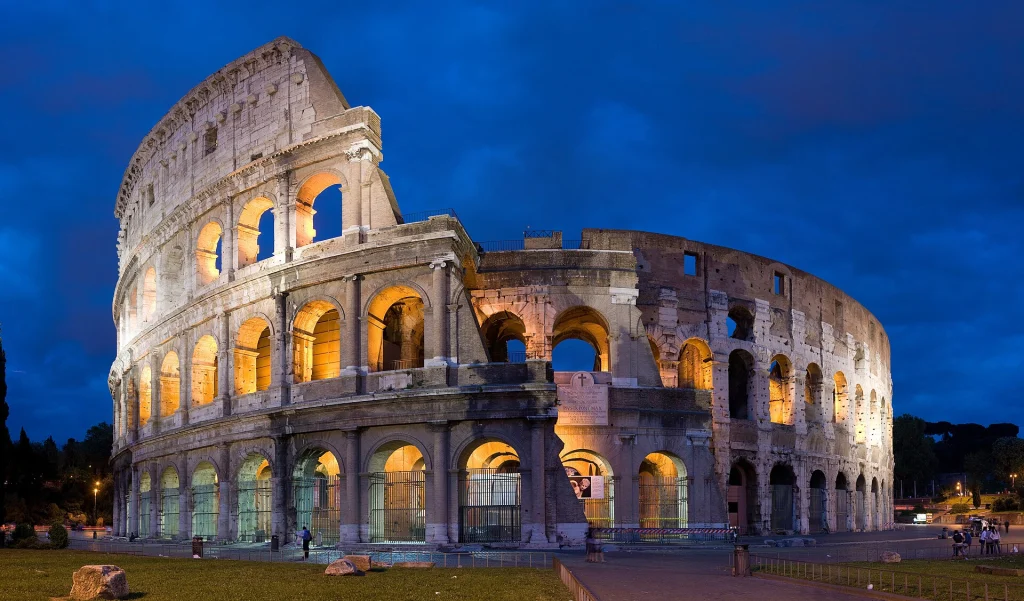The Colosseum in Rome lit up at dusk under a deep blue sky